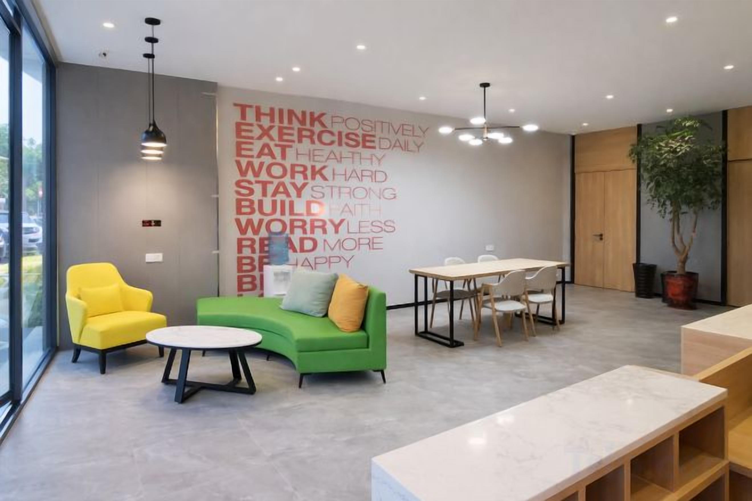 Un área de descanso moderna con un sofá verde, un sillón amarillo y una mesa con sillas.