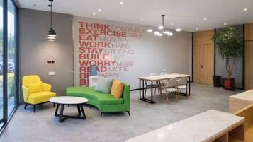 Un área de descanso moderna con un sofá verde, un sillón amarillo y una mesa con sillas.