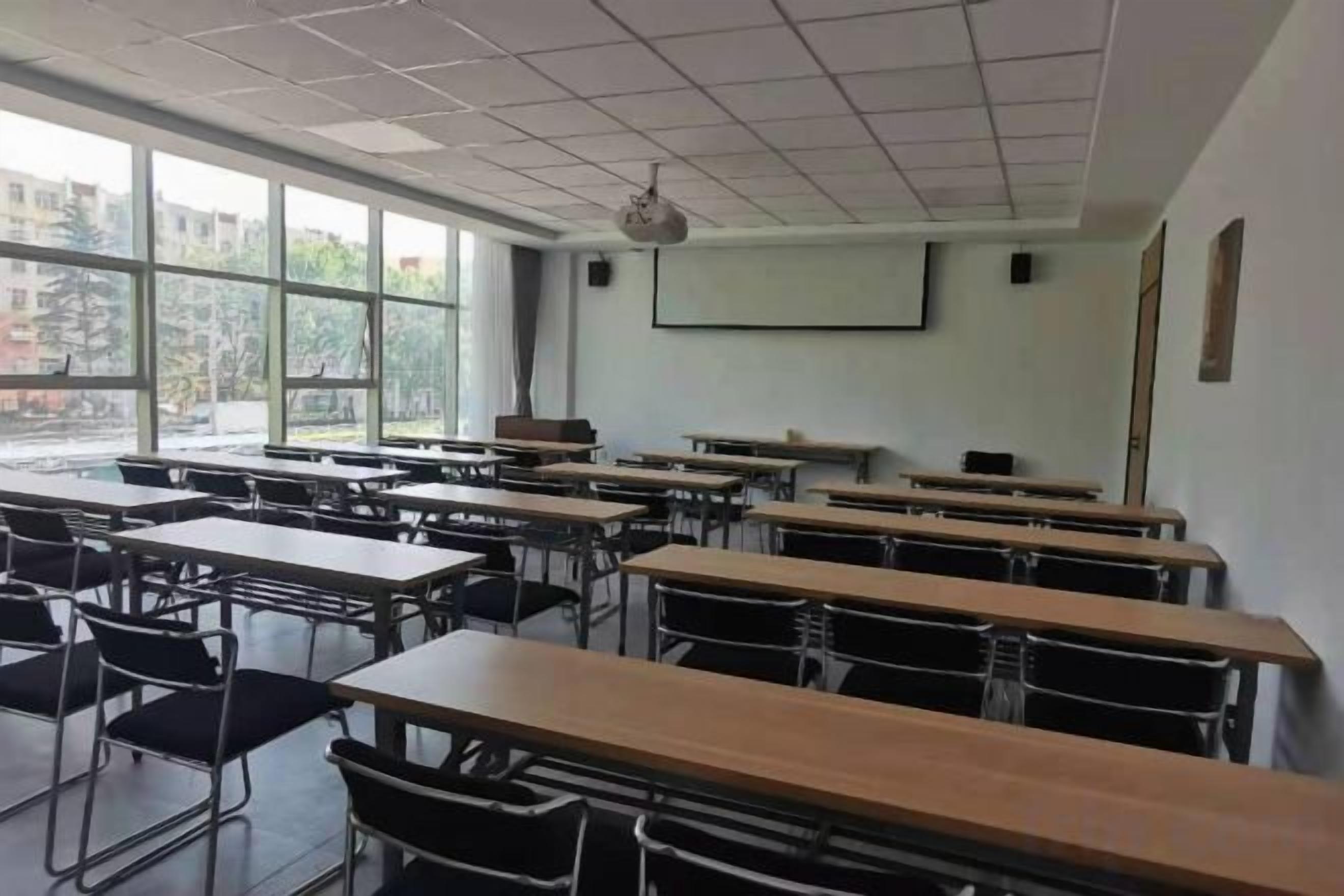A classroom with desks arranged in rows, a projector screen, and a window providing natural light.