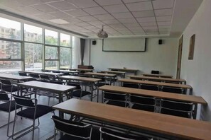 Egy osztályterem, ahol a padok sorokban vannak elrendezve, van egy vetítővászon, és egy ablak, amely természetes fényt biztosít.