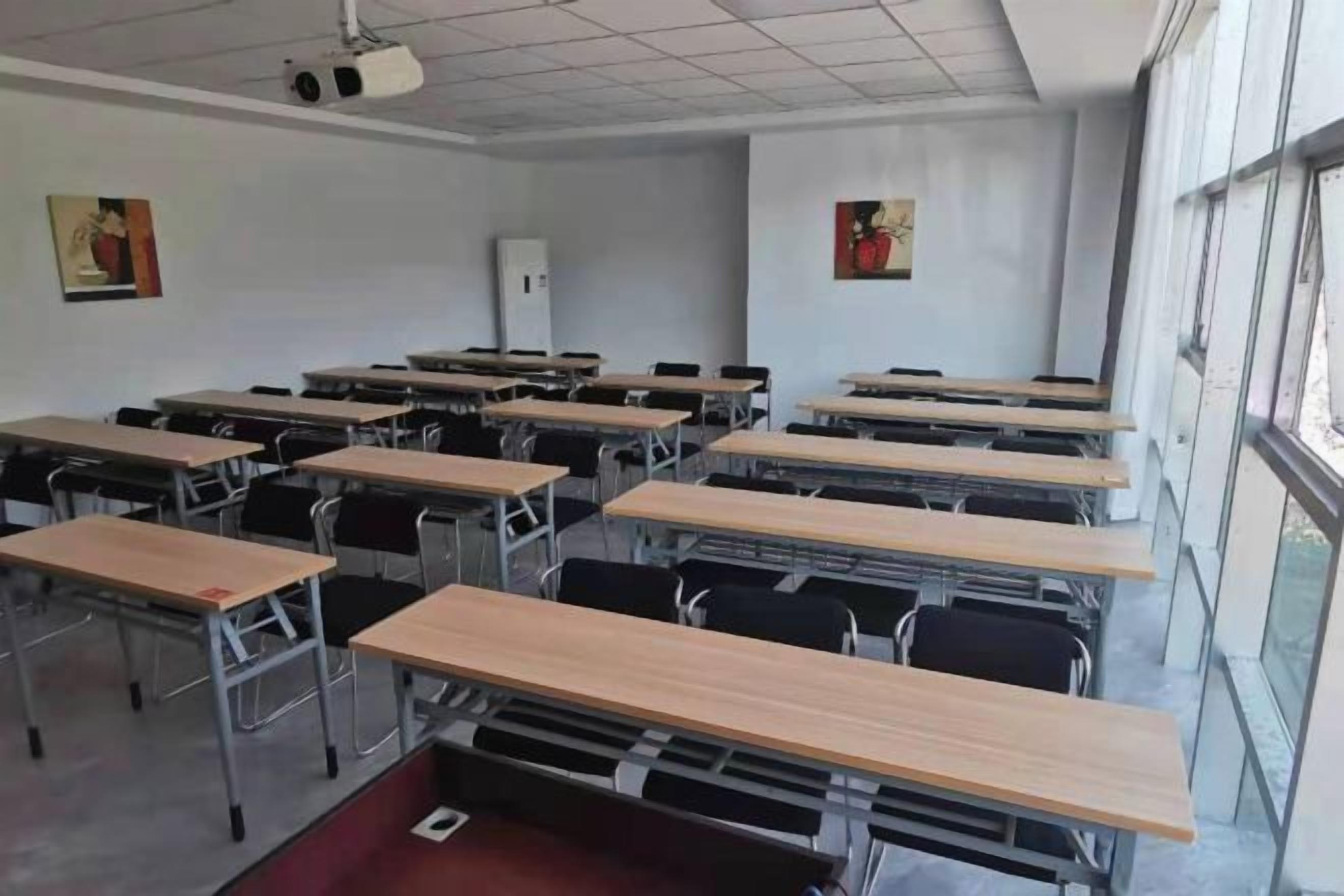 Un aula con filas de escritorios y sillas, un proyector y ventanas.