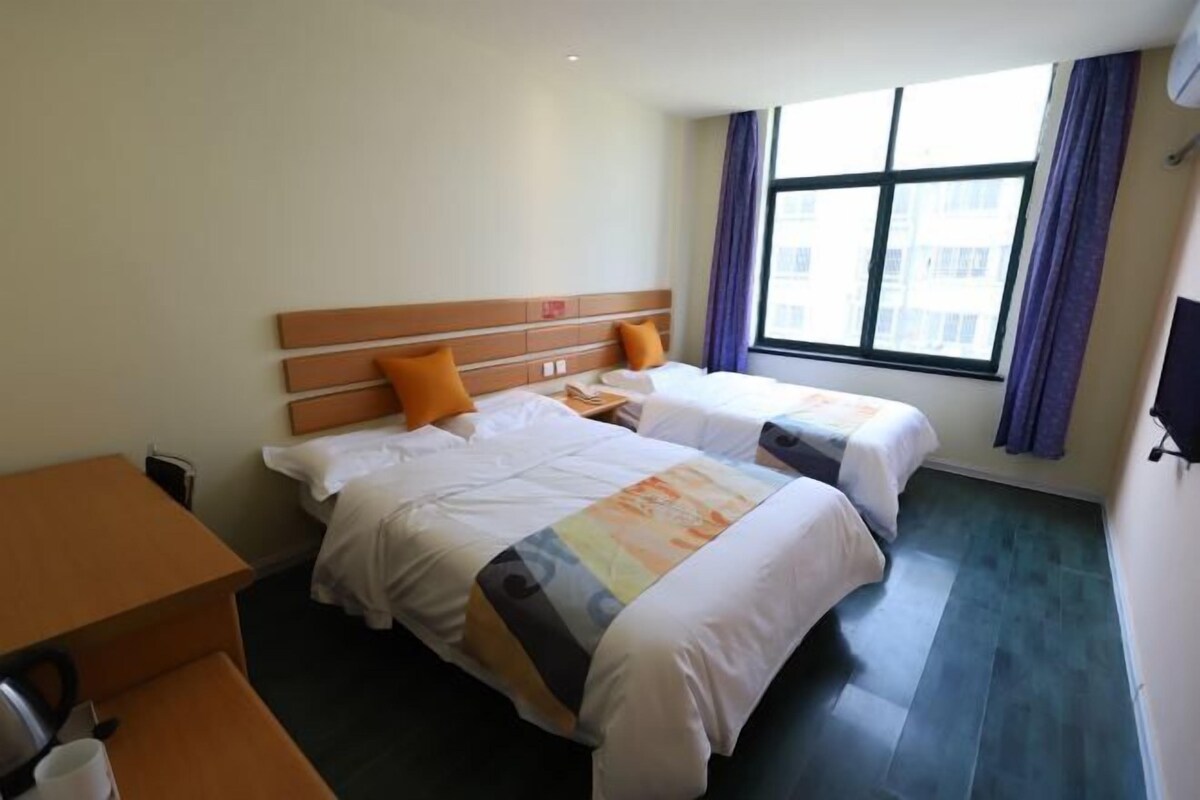 A hotel room with two beds, a desk, and a window with curtains.