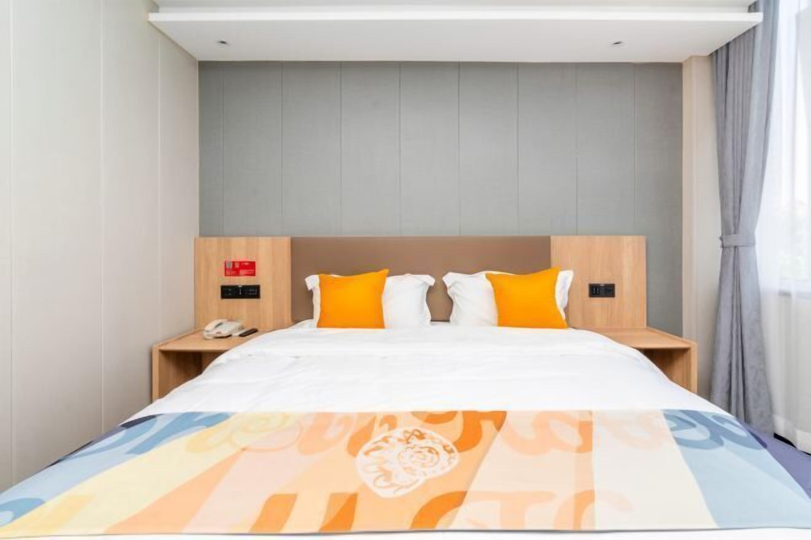 A hotel room with a bed, a nightstand, a phone, and a wall-mounted control panel.