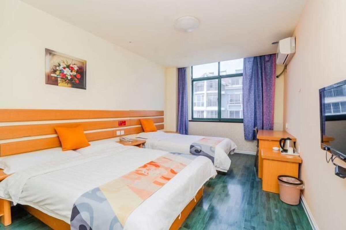 Une chambre d’hôtel avec deux lits, une petite table, un téléviseur et une fenêtre avec des rideaux.
