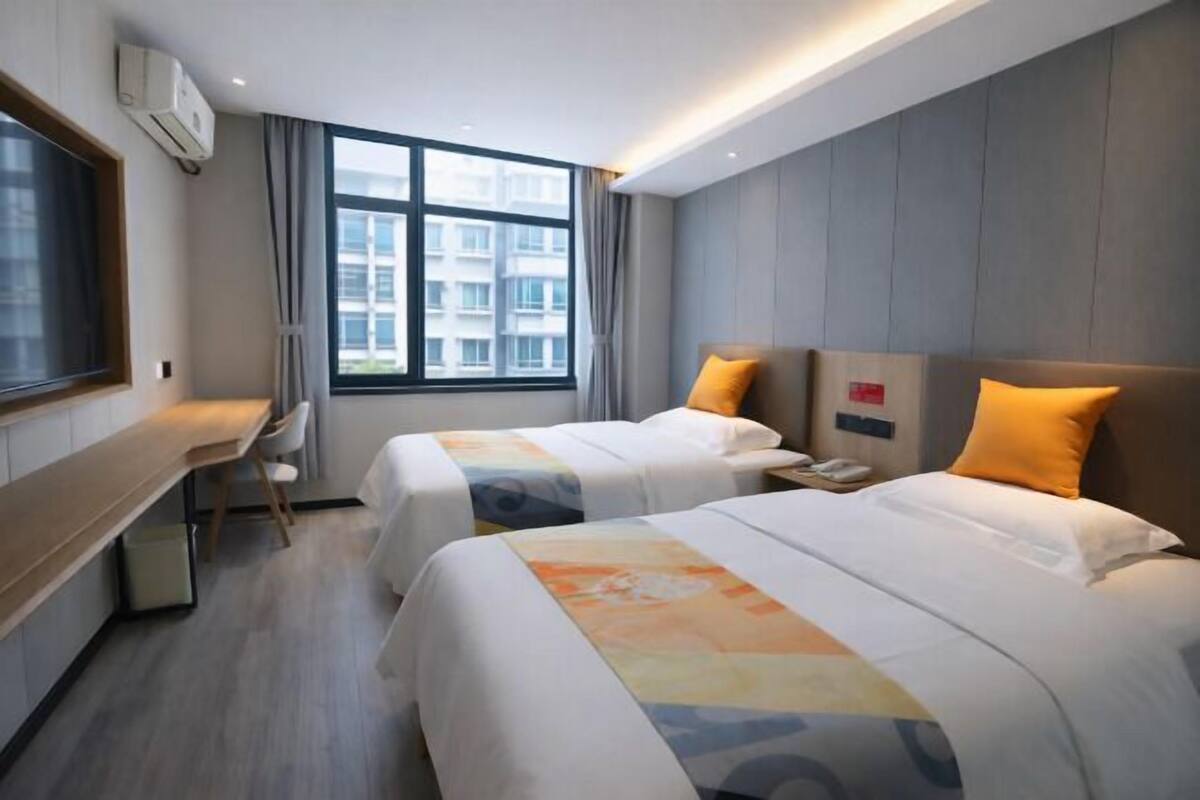 Une chambre d’hôtel avec deux lits, un bureau et une fenêtre donnant sur des immeubles.
