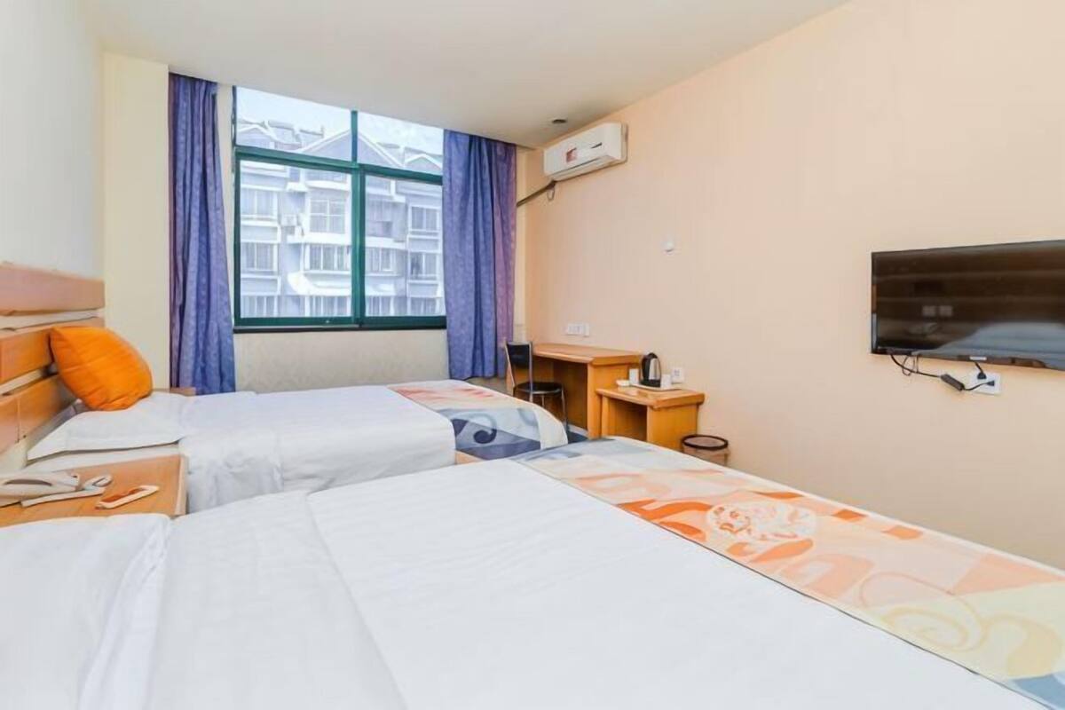 Une chambre d’hôtel avec deux lits, un bureau, une chaise, une télévision et une fenêtre avec des rideaux.