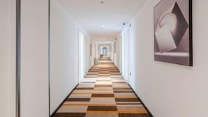 A hotel hallway with a checkered floor, framed artwork on the walls, and a long corridor leading to a distant end. - Shell Hotel (Chengyang Agricultural University Subway Station) (Qingdao)
