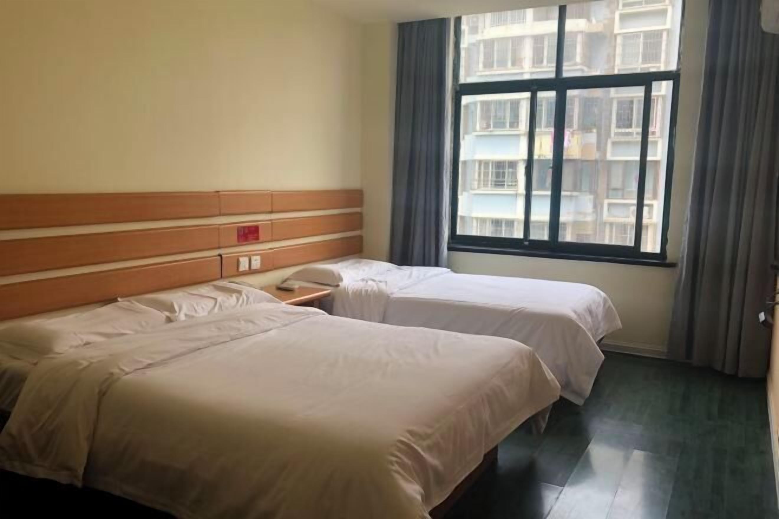 Une chambre d’hôtel avec deux lits, une tête de lit en bois, une fenêtre donnant sur des immeubles et un téléphone sur la table de chevet.