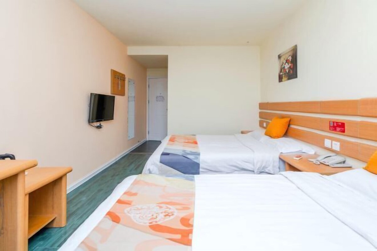 A hotel room with two beds, a TV, a wooden bench, and a door leading to another room.