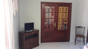 A room with a wooden door, a television on a wooden cabinet, and a wooden chair.