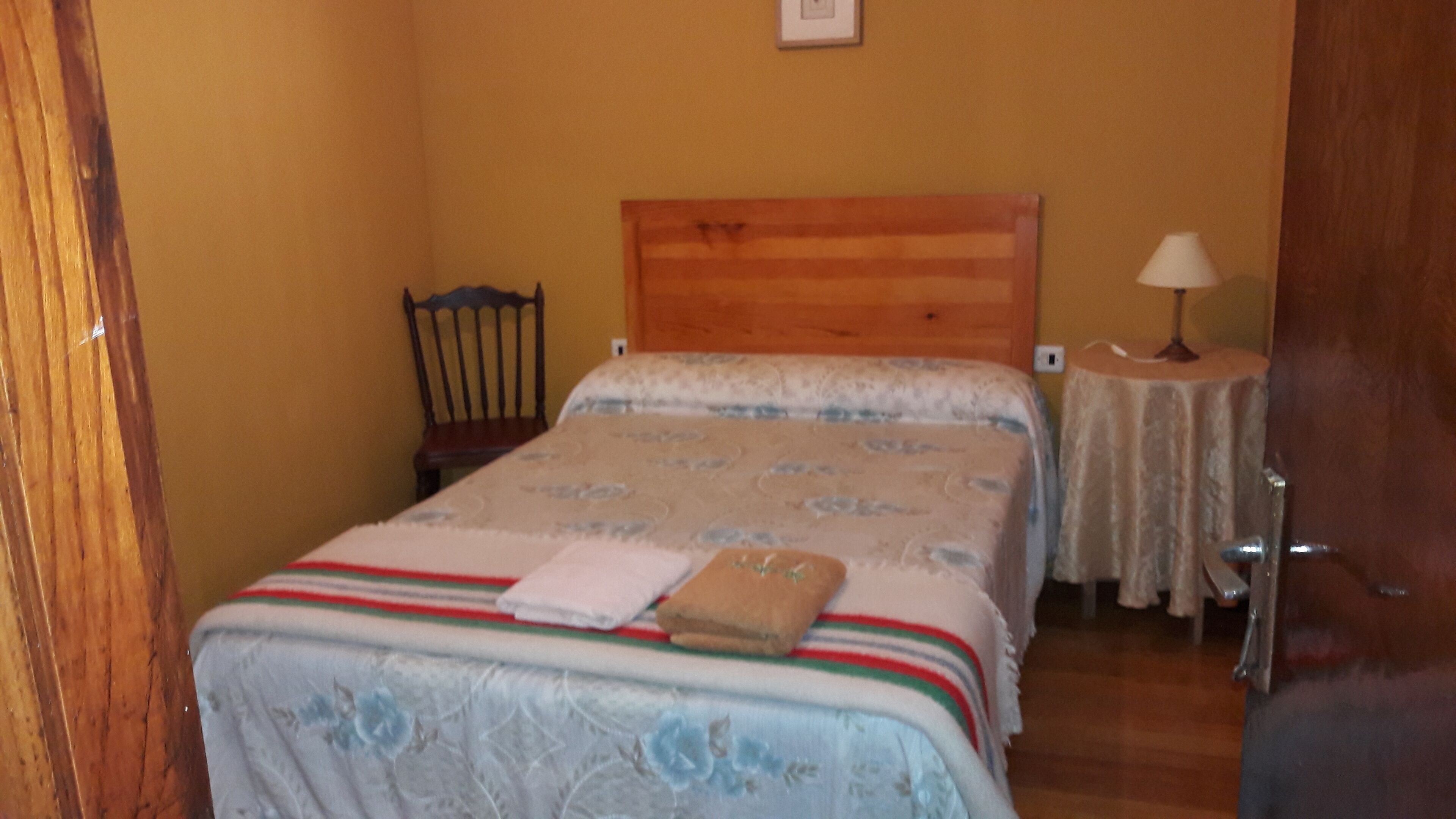 A bedroom with a bed, a chair, a nightstand, and a lamp.