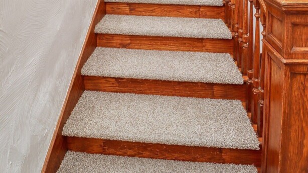 Una escalera de madera con peldaños alfombrados que conduce a una plataforma con una lámpara.