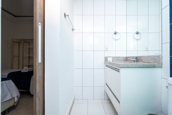 A bathroom with white tiles, a sink with a granite countertop, and a mirror above it. - MFL1802 (Goiânia)