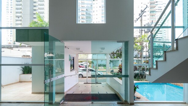 A modern building entrance with a glass door, a pool visible through the window, and a staircase leading to an upper level. - MFL1802 (Goiânia)