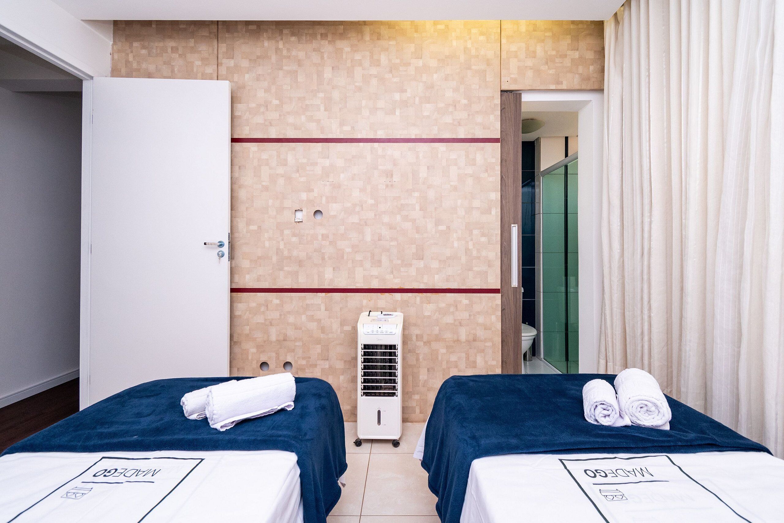A hotel room with two beds, a minibar, a wall-mounted air conditioner, and a bathroom visible through an open door.