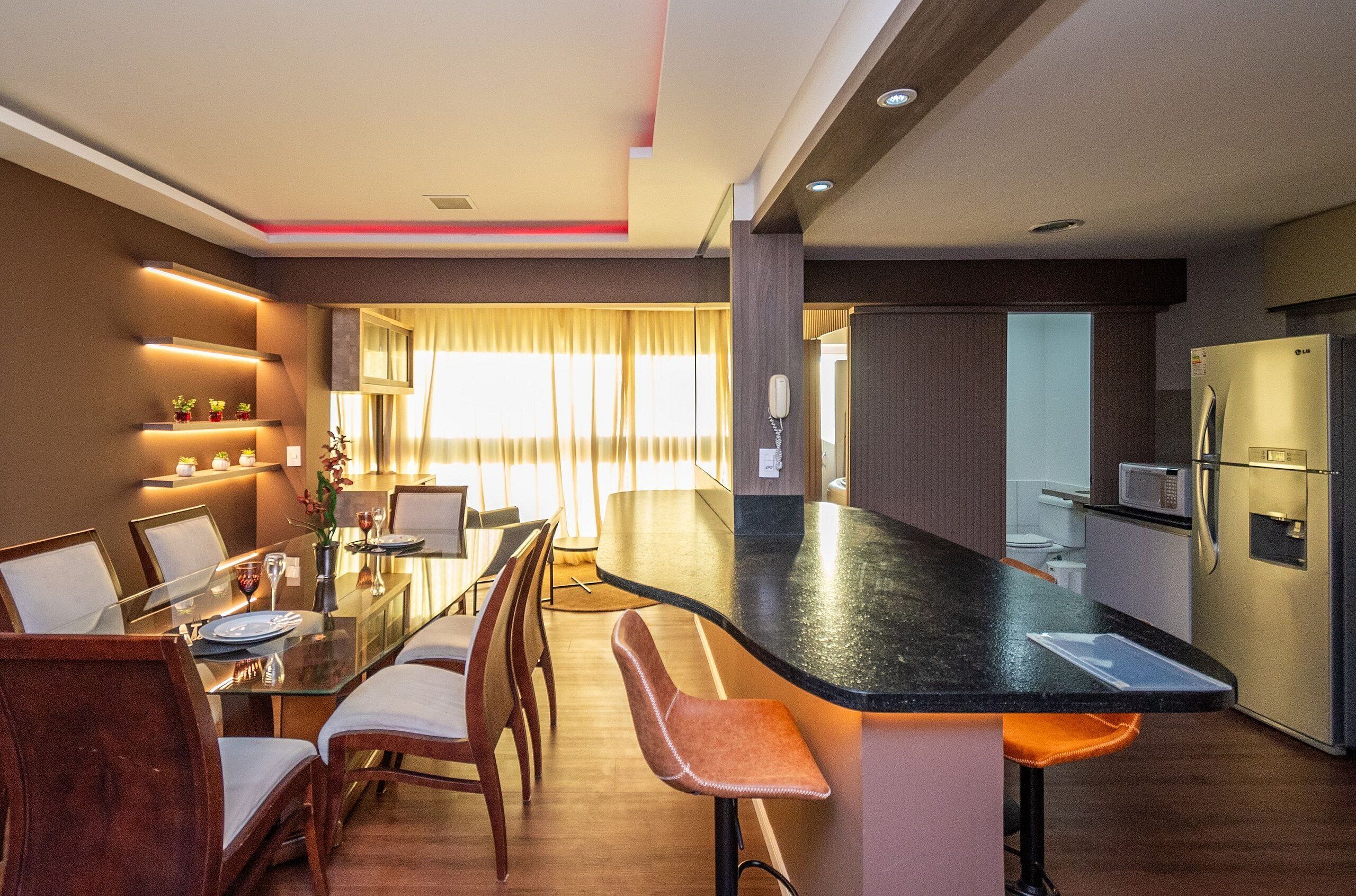 A modern kitchen with a central island, a dining area with a glass table, and a kitchen counter with a microwave and refrigerator.