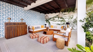 An outdoor seating area with a wooden sofa, ottomans, and a coffee table. - Oceanfront 2BR w/ Two King Beds • Cerritos Beach (Los Cerritos)