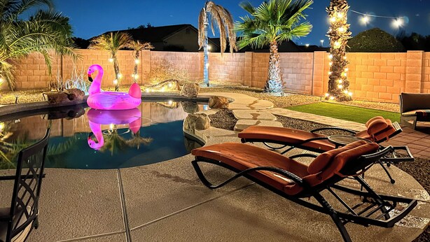 A swimming pool with a pink flamingo float, lounge chairs, and palm trees. - Outdoor Oasis! Family-Friendly North Phoenix Home (Phoenix)