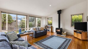 En moderne stue med sofa, sofabord, pejs, fjernsyn og store vinduer med udsigt over naturen.