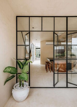 Ein modernes Interieur mit einer großen Topfpflanze, einer Glastrennwand und einem Essbereich mit Holzstühlen.