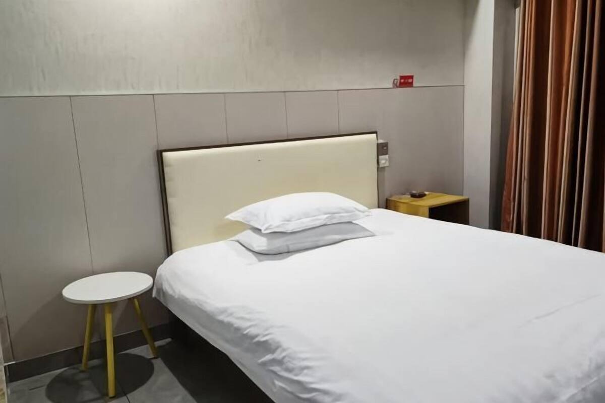 Habitació d'hotel amb un llit, una petita taula de nit, una làmpada penjada a la paret i una cortina.