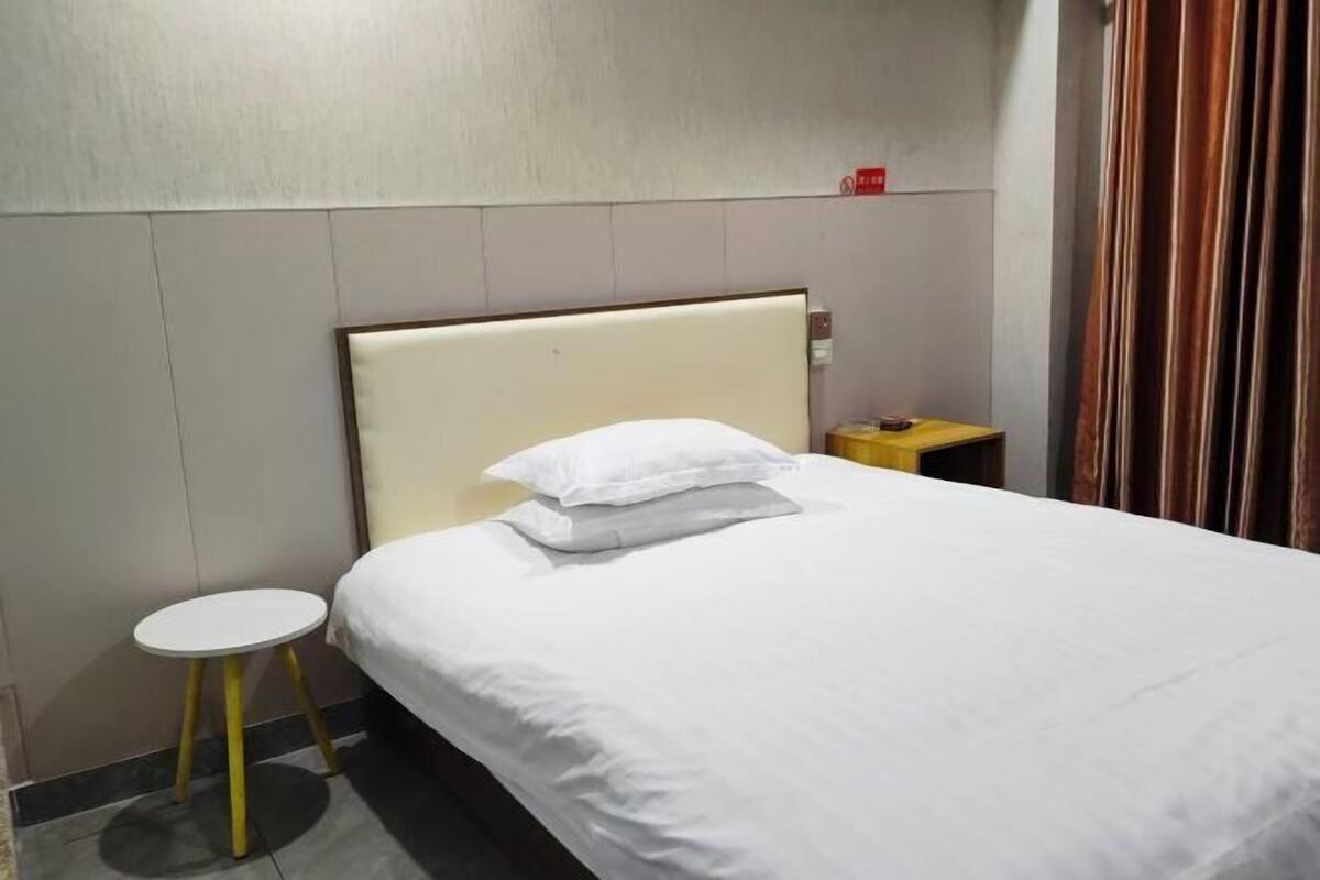 Habitació d'hotel amb un llit, una taula rodona petita, una nitrera i una cortina.
