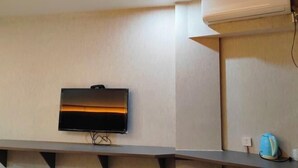 Ein Zimmer mit einem fest installierten Flachbildfernseher, einer integrierten Klimaanlage und einem Regal mit Wasserkocher und Tasse.