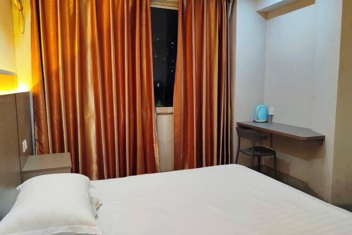 Habitació d'hotel amb llit, escriptori, cadira i finestra amb cortines.
