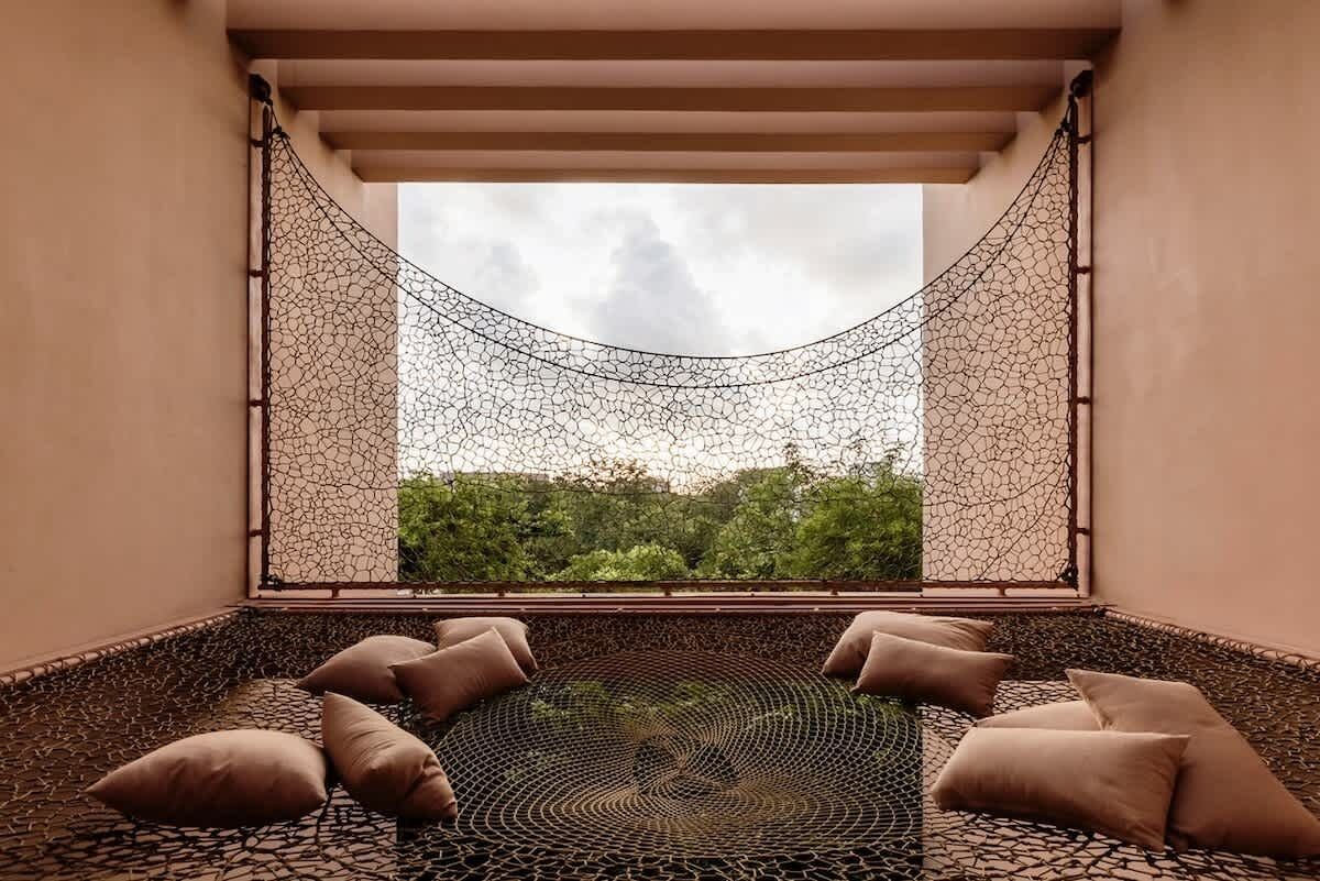 A hammock with a view of greenery, a patterned floor, and beige cushions.