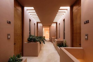 A hallway with a central plant, wooden doors, and a light fixture on the ceiling.