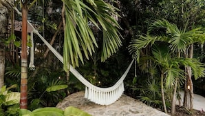 Un hamac dans un jardin luxuriant, avec un sol en pierre et une végétation tropicale dense.