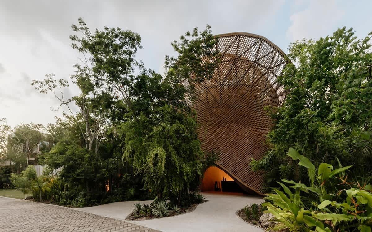 Un edificio moderno con una fachada de celosía distintiva, rodeado de exuberante vegetación.