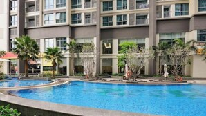 A multi-story hotel with a central swimming pool surrounded by palm trees and lounge chairs. - O Clean Home, Vinhomes Central Park (Ho Chi Minh City)