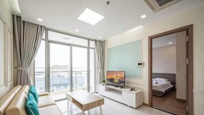 A modern hotel room with a sofa, a TV on a white console, a balcony with curtains, and a bed with a white duvet. - O Clean Home, Vinhomes Central Park (Ho Chi Minh City)
