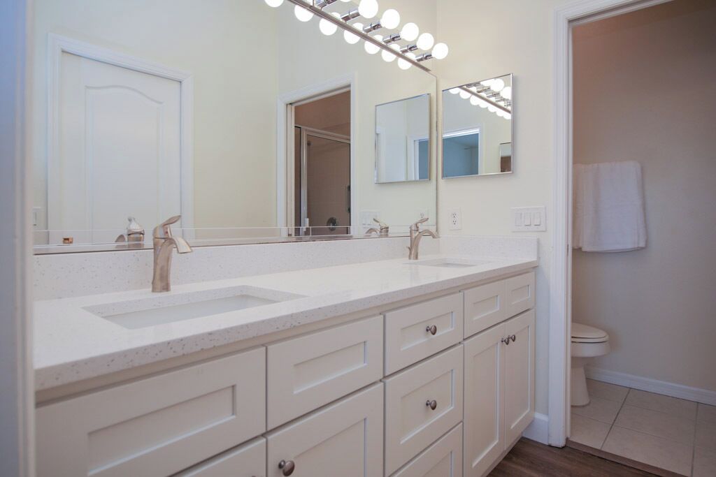 Une salle de bain avec un meuble-lavabo à deux vasques, un grand miroir avec éclairage intégré et des toilettes.