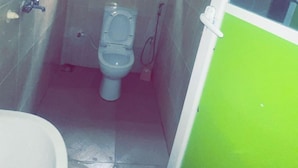A small, narrow bathroom with a toilet, a shower, and a window. - Ajoke Hotel (Abeokuta)