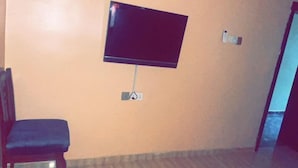 A room with a flat-screen TV mounted on the wall, a wooden chair, and a patterned carpet. - Ajoke Hotel (Abeokuta)