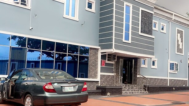 A building with a blue facade, large windows, and a car parked in front. - Ajoke Hotel (Abeokuta)
