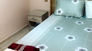 A bedroom with a bed, a nightstand, an air conditioning unit, and a window with curtains. - Ajoke Hotel (Abeokuta)