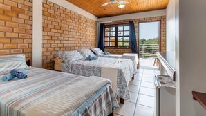 Una habitación con dos camas, techo de madera, paredes de ladrillo, una ventana con cortinas y un balcón.