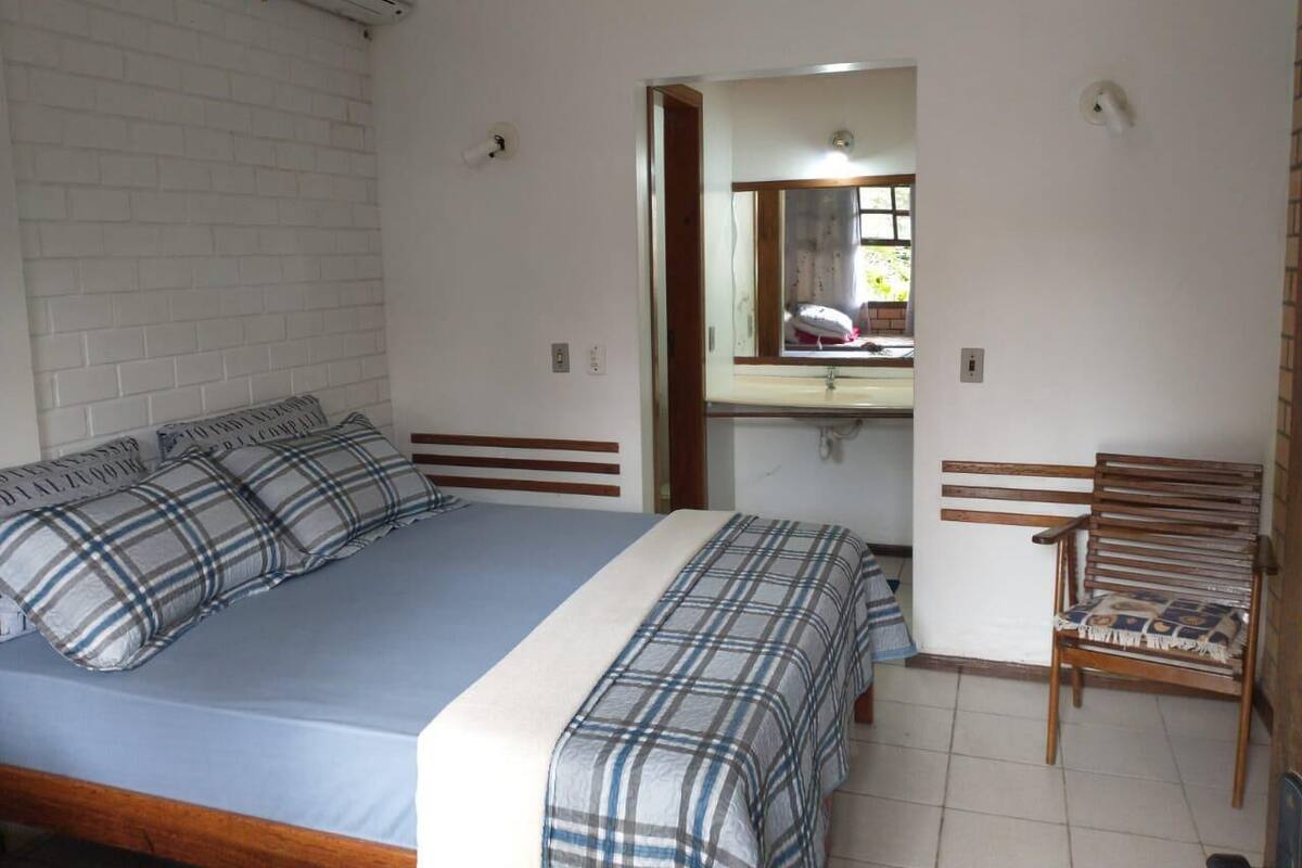 A bedroom with a bed, a chair, a mirror, and a window.