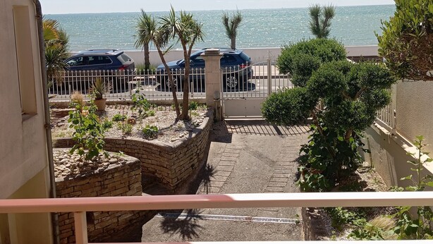 Un balcon avec vue sur la mer, un espace de stationnement et quelques espaces verts.