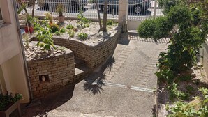 Un chemin pavé mène à une entrée fermée par un portail, d’où l’on peut admirer la mer.