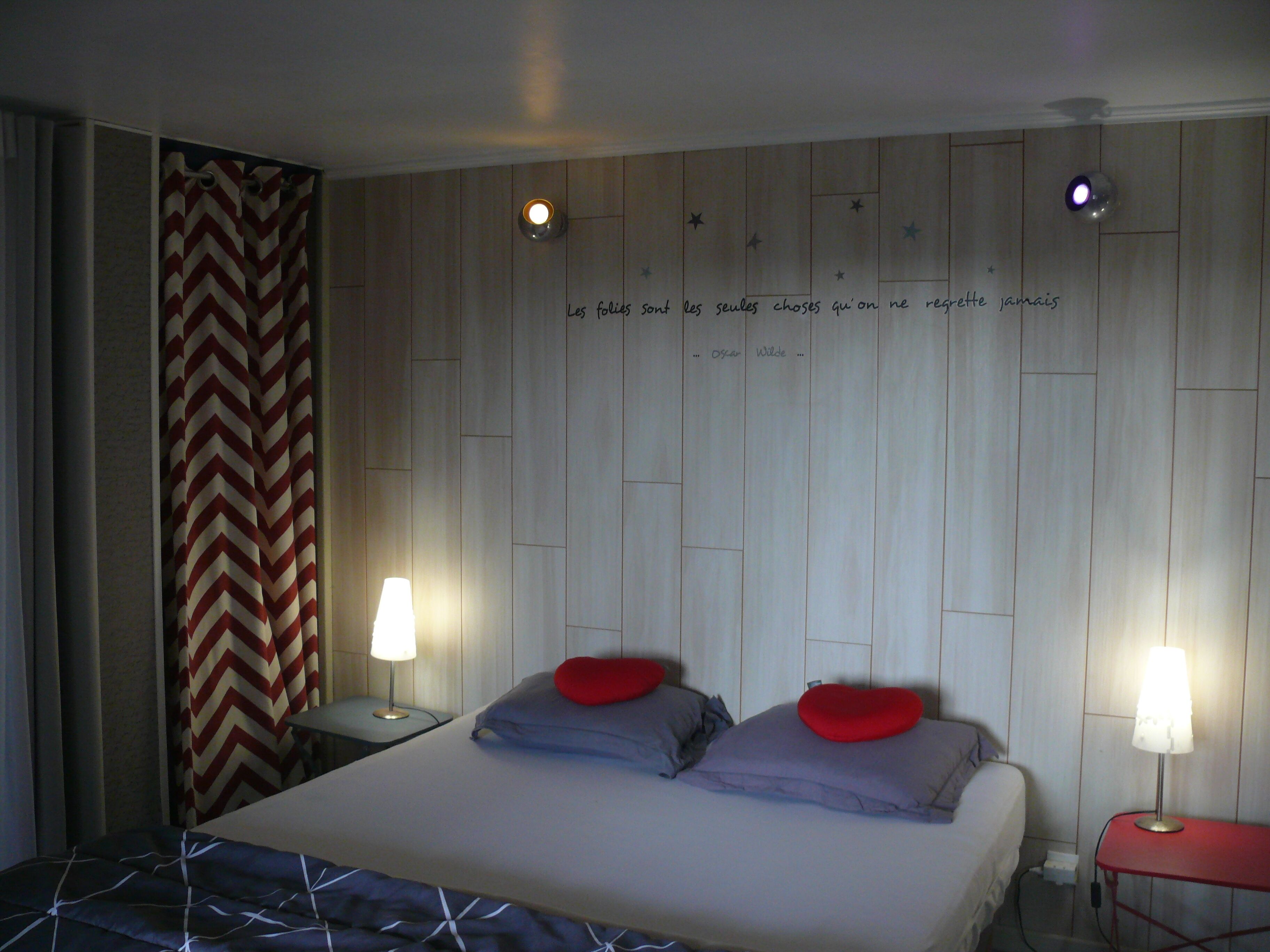 A hotel room with a bed, two bedside tables, and a wall with a quote.