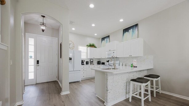 A modern kitchen with white cabinetry, a central island with stools, and recessed ceiling lights. - HOME SWEET HOME ! COMFY 4 BED 4 BATH SLEEPING 10  PRIVATE TUSCAN HILLS COMMUNITY (Davenport)