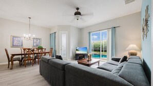A modern living room with a grey sectional sofa, a wooden dining table with chairs, a flat-screen TV, and a ceiling fan. - HOME SWEET HOME ! COMFY 4 BED 4 BATH SLEEPING 10  PRIVATE TUSCAN HILLS COMMUNITY (Davenport)
