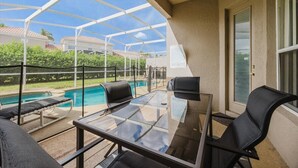A covered outdoor area with a glass table and chairs, a pool, and a view of a residential neighborhood. - HOME SWEET HOME ! COMFY 4 BED 4 BATH SLEEPING 10  PRIVATE TUSCAN HILLS COMMUNITY (Davenport)