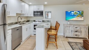 A modern kitchen with white cabinets, stainless steel appliances, a marble countertop, and a dining area with wicker chairs.