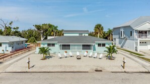 A motel with a central building and a parking area with white chairs and a palm tree.