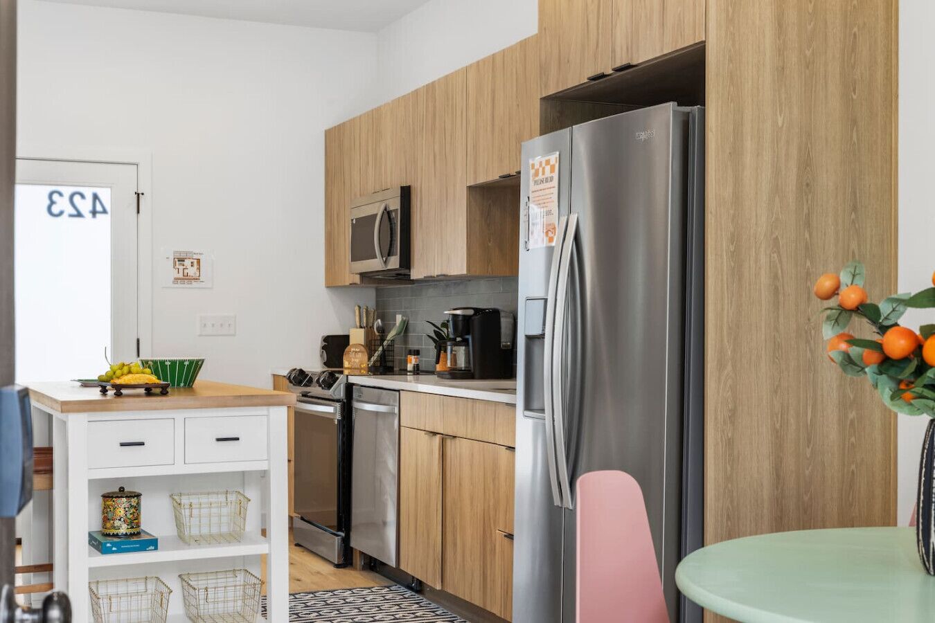 A modern kitchen with wooden cabinets, a stainless steel refrigerator, a microwave, and a dining area with a table and chairs.